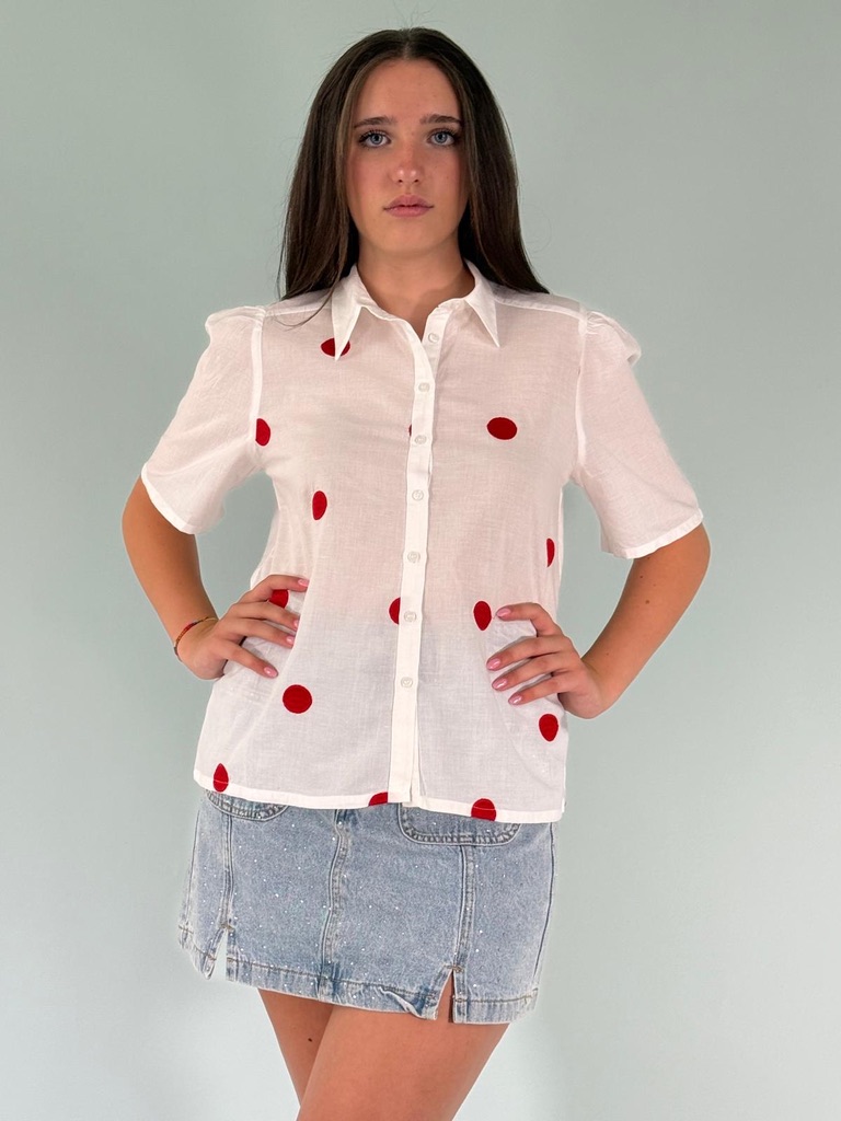 Camicia maniche corte a sbuffo con colletto a revers allacciata sul davanti con bottoni.Dettaglio dei pois rossi.