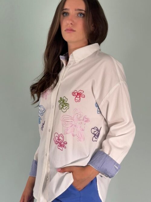 Camicia ricamata, con il dettaglio del polsino con risvolto a righe bianche e blu. Allacciata sul davanti con bottoni a forma di fiore.