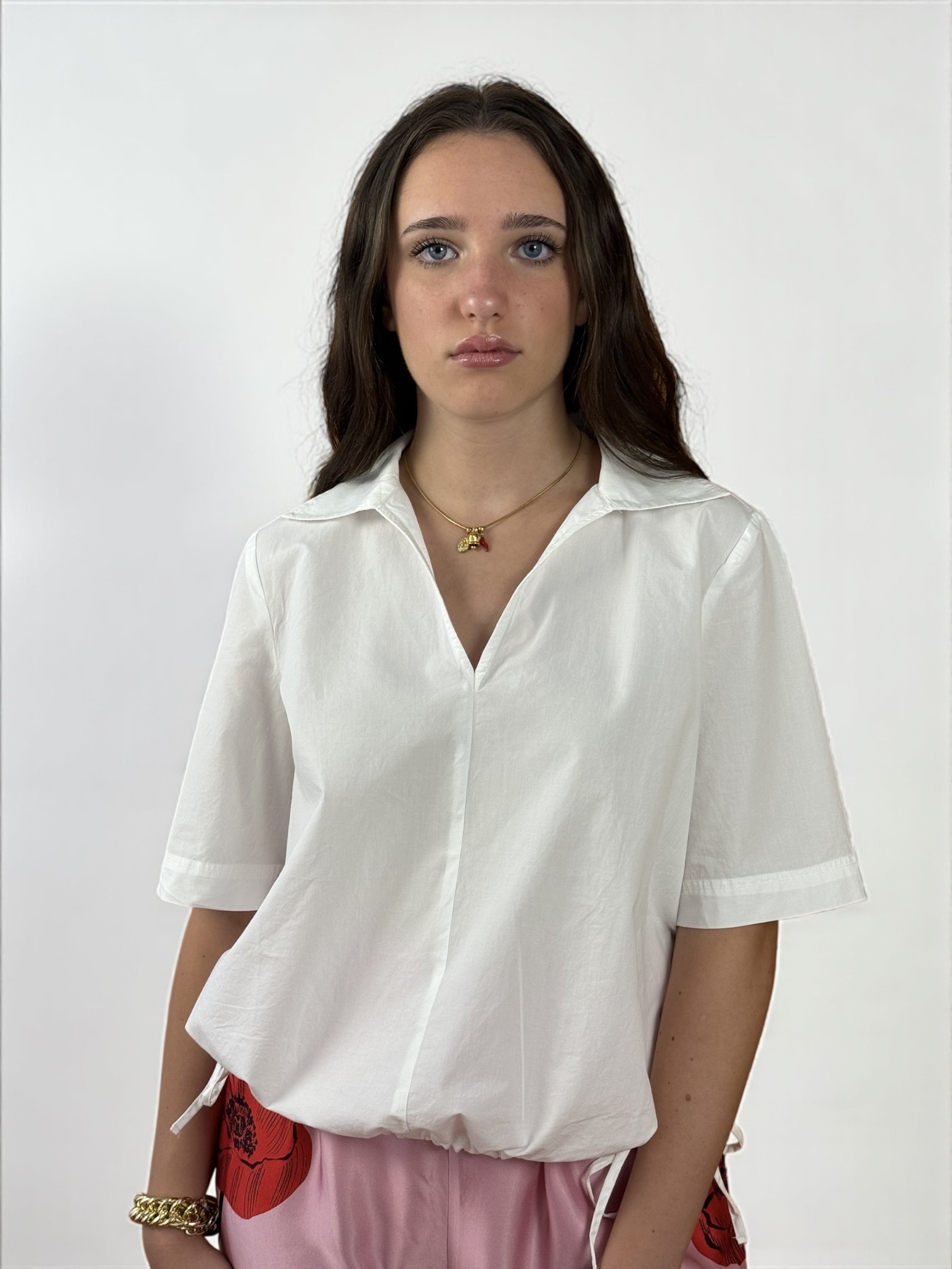 Blusa a maniche corte con scollatura a V e colletto. Presenta due spacchetti laterali e due laccietti che creano un effetto arricciato.