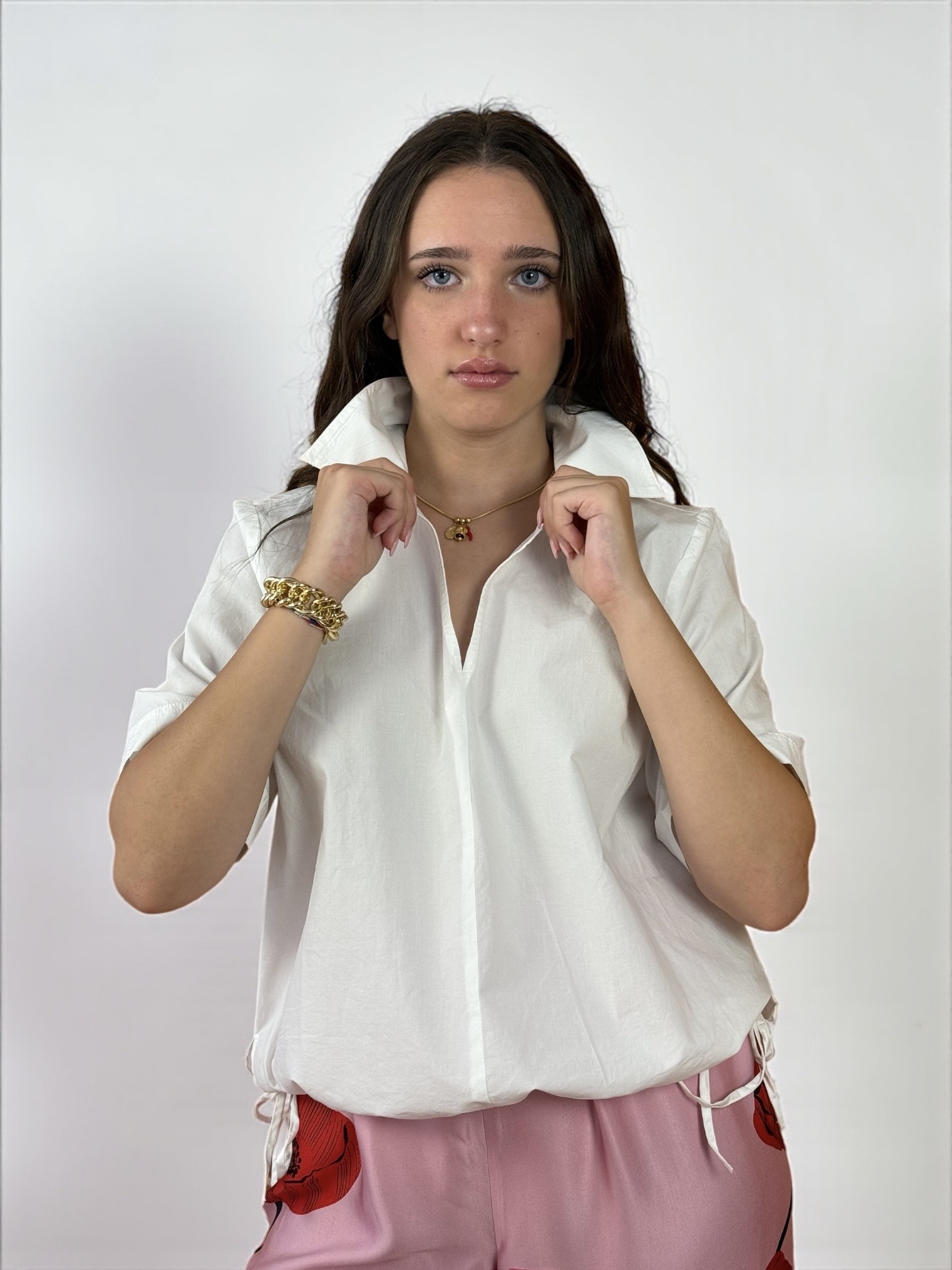 Blusa a maniche corte con scollatura a V e colletto. Presenta due spacchetti laterali e due laccietti che creano un effetto arricciato.