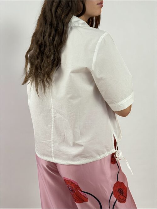 Blusa a maniche corte con scollatura a V e colletto. Presenta due spacchetti laterali e due laccietti che creano un effetto arricciato.