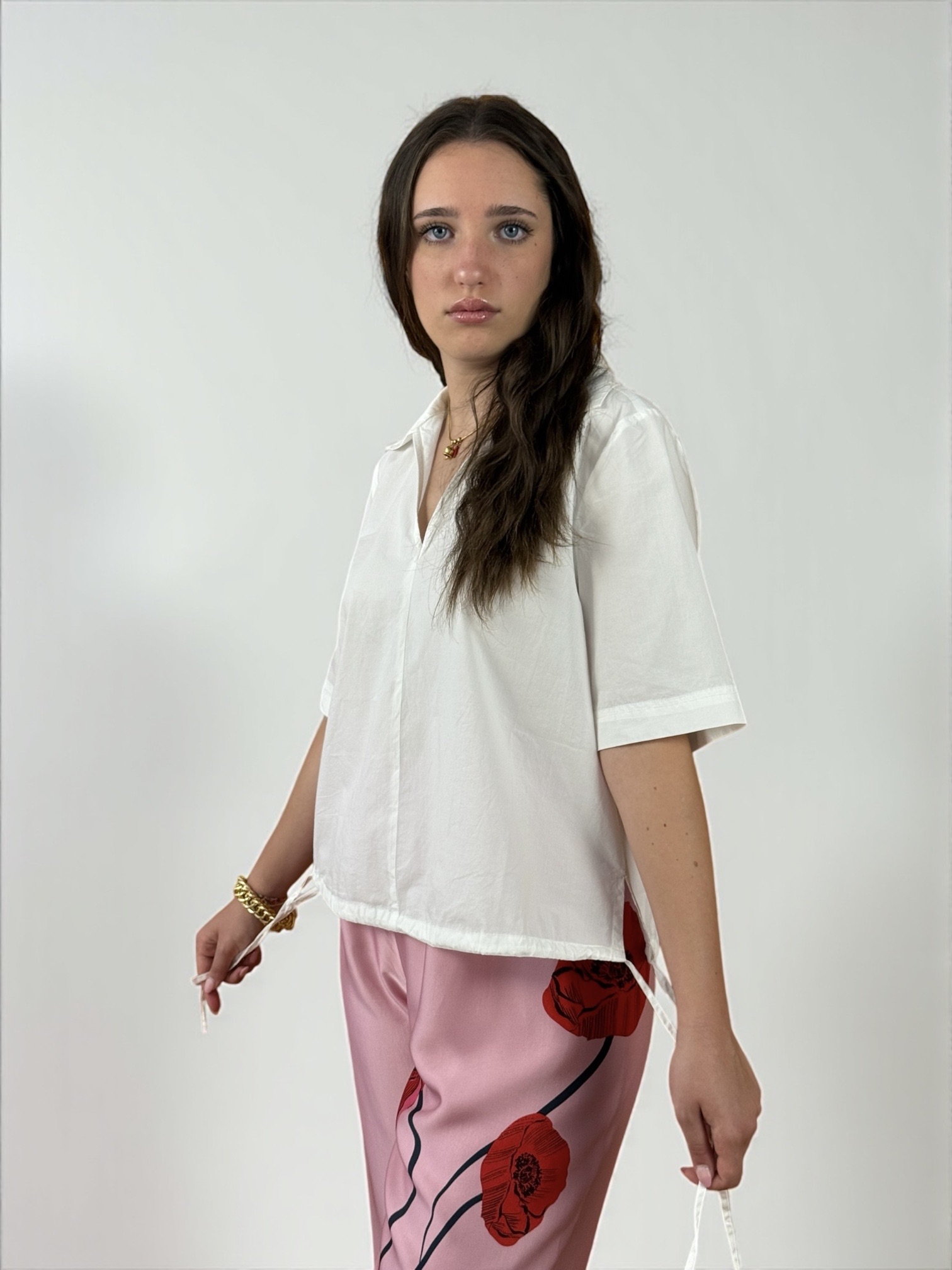 Blusa a maniche corte con scollatura a V e colletto. Presenta due spacchetti laterali e due laccietti che creano un effetto arricciato.