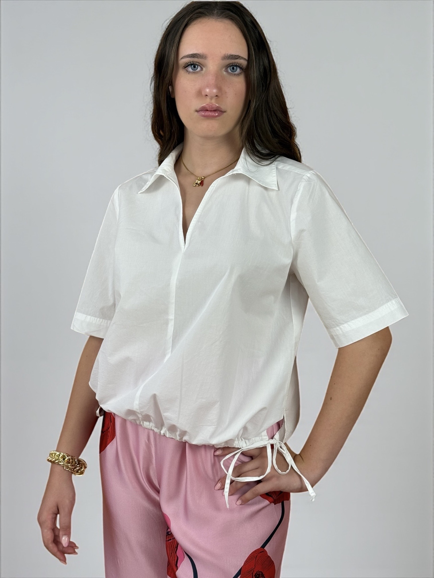 Blusa a maniche corte con scollatura a V e colletto. Presenta due spacchetti laterali e due laccietti che creano un effetto arricciato.